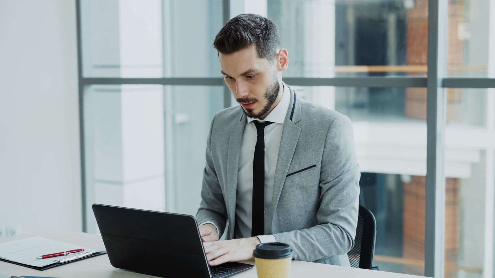 Nhân viên văn phòng mặc vest ngồi làm việc với laptop trong văn phòng có tường kính