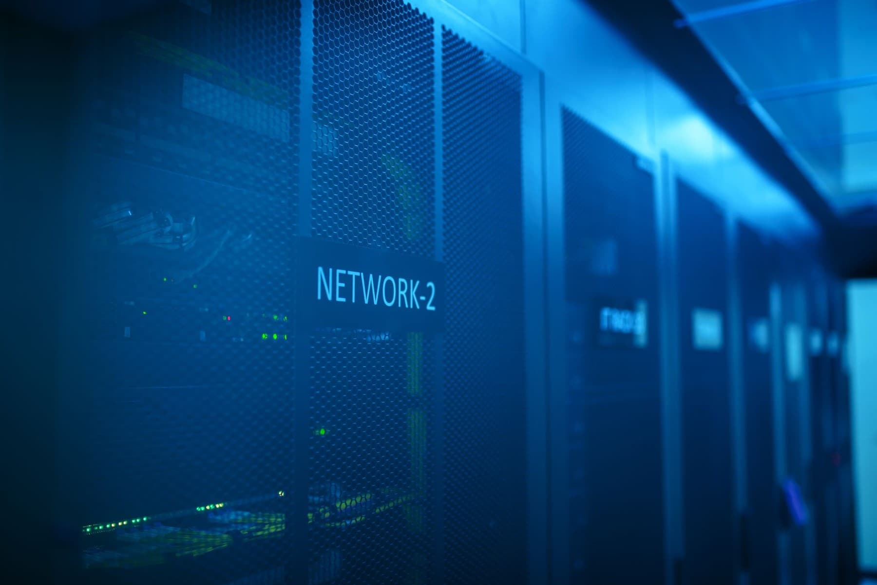 Dãy tủ rack cửa lưới trong phòng máy chủ được chiếu ánh sáng xanh lam, nhãn NETWORK-2 trên cửa tủ